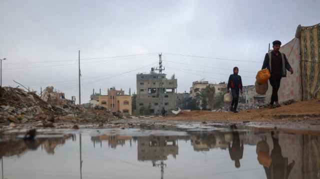 Des personnes déplacées passent devant une mare d'eau de pluie près des tentes du camp de réfugiés de Bureij, dans le centre de la bande de Gaza, le 24 novembre 2024.