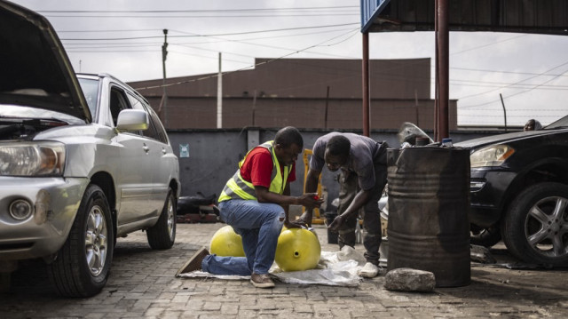 Jide Fashetire, fondateur de City Mechanic, et un mécanicien installent une bouteille de gaz utilisée pour convertir les voitures à la combustion du gaz à City Mechanic, un centre de gaz naturel comprimé (GNC) à Lagos, le 12 novembre 2024.