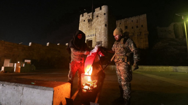 Des combattants anti-gouvernementaux se réchauffent près d'un feu de joie devant la citadelle d'Alep, le 30 novembre 2024.