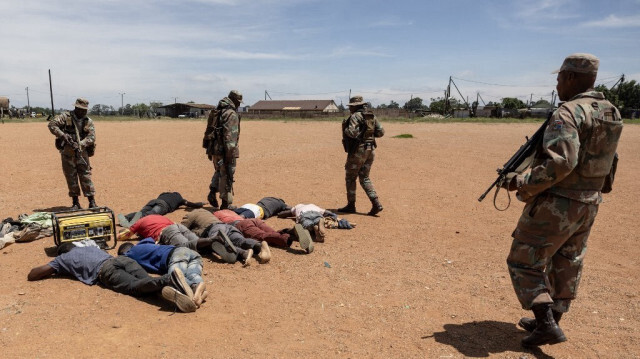 Des soldats de la South African National Defence Force (SANDF) se tiennent à côté de mineurs informels présumés, communément appelés "zama zamas" ("ceux qui essaient" en langue zouloue) lors de l'opération "Shanela" dans le quartier informel de Soul City, près de Kagiso, le 14 décembre 2023.