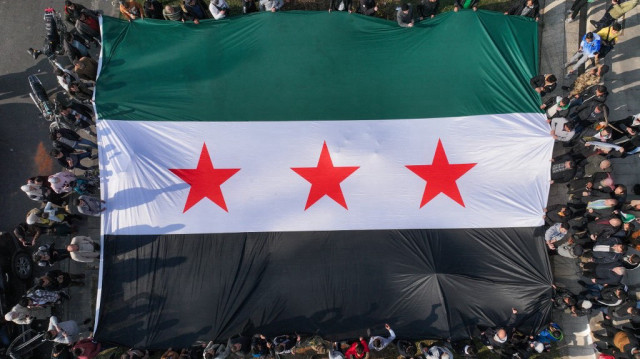 Des syriens tiennent un grand drapeau de l'opposition syrienne sur la place des Omeyyades à Damas, le 9 décembre 2024. 