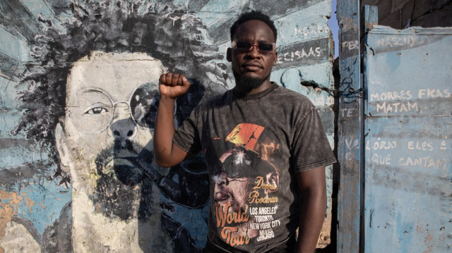 Higino Fumo, 32 ans, connu dans le monde du rap sous le nom de "Nikotina" lève le poing en posant pour un portrait à côté d'une peinture murale à la mémoire du rappeur Mano Azagaia et critique du Frelimo, décédé en 2023 à Maputo le 3 décembre 2024. 