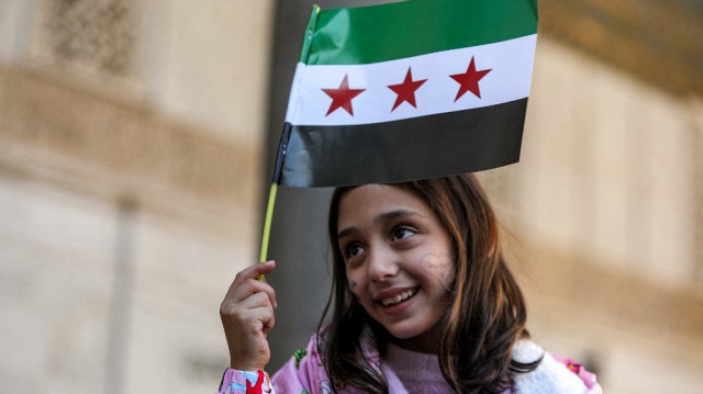 Une petite fille syrienne tient le nouveau drapeau de Syrie avant la première prière musulmane hebdomadaire du vendredi depuis la chute du régime de Bachar al-Assad, dans la mosquée omeyyade du VIIIe siècle de la vieille ville de Damas, le 13 décembre 2024.