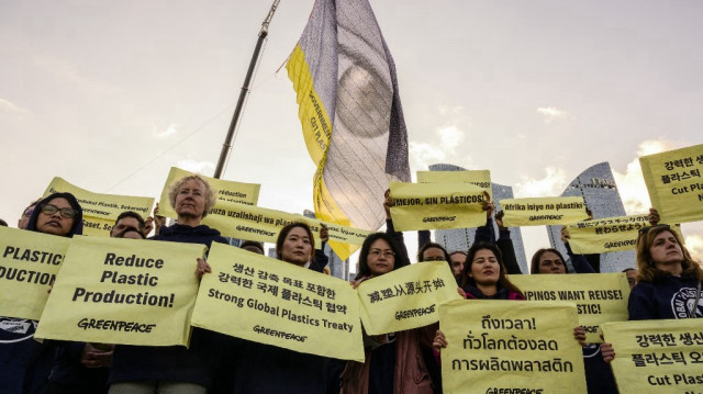 Un drapeau avec un œil et l'inscription "Gouvernements, le monde regarde, réduisez la production de plastique maintenant" est affiché au-dessus de militants de Greenpeace tenant des pancartes à Busan le 25 novembre 2024, avant l'ouverture de la cinquième session du Comité intergouvernemental de négociation sur la pollution plastique de l'ONU (INC-5) dans un lieu voisin.