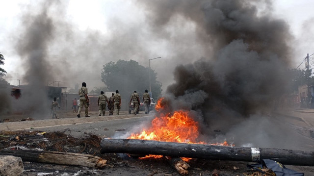 Des piétons passent devant une barricade en feu à Maputo au Mozambique, le 24 décembre 2024.