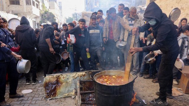 Un volontaire remue un pot de nourriture alors que les Palestiniens attendent de recevoir des portions d'aide humanitaire, dans le camp d'al-Shati près de la ville de Gaza, le 26 décembre 2024.