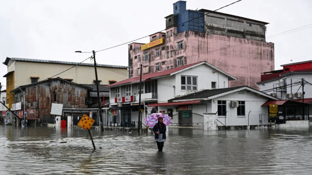 Une femme patauge dans une rue inondée lors de fortes pluies à Pasir Puteh, dans l'État malaisien de Kelantan, le 30 novembre 2024.