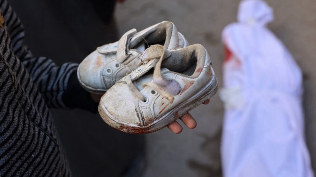 Un enfant Palestinien tient les chaussures tachées de sang d'un autre enfant qui a été tué par une frappe israélienne dans la ville de Gaza, alors que le corps est préparé pour l'enterrement, à l'hôpital arabe Al-Ahli, le 5 décembre 2024.