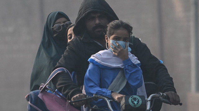 Un homme conduit une moto transportant des écoliers au milieu d'un épais smog à Lahore, le 21 novembre 2024. 