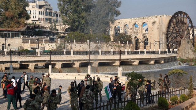 Des combattants anti-gouvernementaux syriens se rassemblent parmi des civils près de l'une des roues à eau de Hama, ou norias, après la prise de la ville de Hama par les forces armées, le 6 décembre 2024. Les forces rebelles qui mènent une offensive éclair en Syrie ont pour objectif de renverser le régime du président Bachar al-Assad, a déclaré leur chef dans une interview publiée le 6 décembre. En un peu plus d'une semaine, l'offensive a vu la deuxième ville de Syrie, Alep, et la ville stratégique de Hama échapper au contrôle d'Assad pour la première fois depuis le début de la guerre civile en 2011.