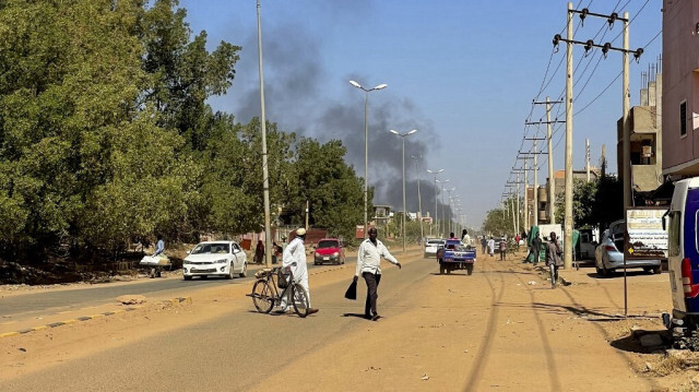 Des personnes déplacées par le conflit au Soudan marchent le long d'une route alors que de la fumée s'élève au loin pendant les affrontements à Wad Madani, capitale de l'État d'al-Jazirah, le 16 décembre 2023.