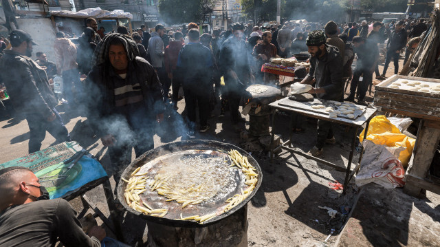 Des vendeurs préparant du pain et des pommes de terre frites pour les vendre comme nourriture de rue le long d'une rue principale bondée à Rafah dans le sud de la bande de Gaza le 8 février 2024.