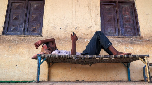 Un homme consulte son téléphone tout en étant allongé sur un lit de paille à l'extérieur d'une salle de classe dans une école qui a été transformée en abri pour les personnes déplacées par le conflit dans la ville frontalière du nord du Soudan de Wadi Halfa, près de l'Égypte, le 11 septembre 2023. 