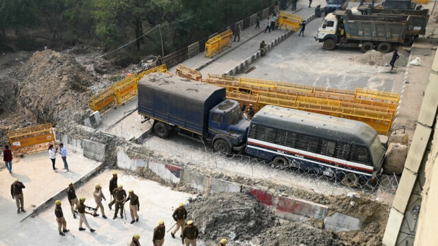 Le personnel de police garde à côté d'une barrière et de véhicules bloquant une route pour empêcher les agriculteurs de protester pour exiger des prix minimaux des cultures de marcher vers la capitale indienne à la frontière Delhi-Uttar Pradesh dans le Ghazipur le 14 février 2024.