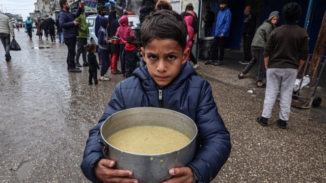 Un enfant palestinien déplacé de force à cause des bombardements de l'armée d'occupation israélienne, porte une ration de soupe, distribuée par des bénévoles à Rafah, dans le sud de la Bande de Gaza, le 18 février 2024.