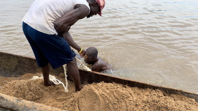 Saturnin Yenzia (G) tire une corde pour mettre un seau de sable sur sa pirogue sur le fleuve Ubangi à Bangui le 8 novembre 2023. 