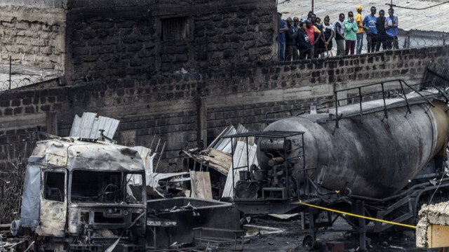 Des gens se tiennent sur les murs d'un bâtiment endommagé pour voir les débris de troncs brûlés et de camions-citernes, le lendemain d'une explosion de gaz ayant causé de graves dommages dans la région d'Embakasi à Nairobi le 2 février 2024.