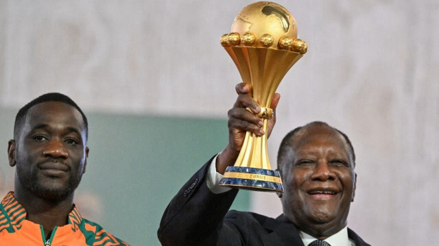 Le président ivoirien Alassane Ouattara tient le trophée de la Coupe d'Afrique des Nations aux côtés de l'entraîneur de l'équipe Emerse Fae (à gauche), lors d'une réception au palais présidentiel à Abidjan, le 13 février 2024 après que la Côte d'Ivoire a remporté la CAN 2024.