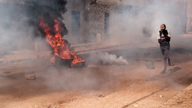 Un manifestant fuit la fumée des gaz lacrymogènes devant un feu lors d'affrontements avec la police en marge d'une manifestation contre le report à la dernière minute des élections présidentielles à Dakar, le 9 février 2024. 