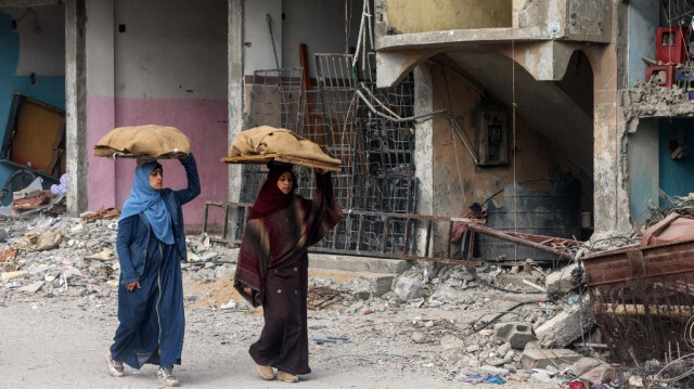 Des femmes portent des pains sur la tête alors qu'elles marchent devant un bâtiment endommagé par les bombardements israéliens à Rafah, dans le sud de la bande de Gaza, le 25 février 2024.