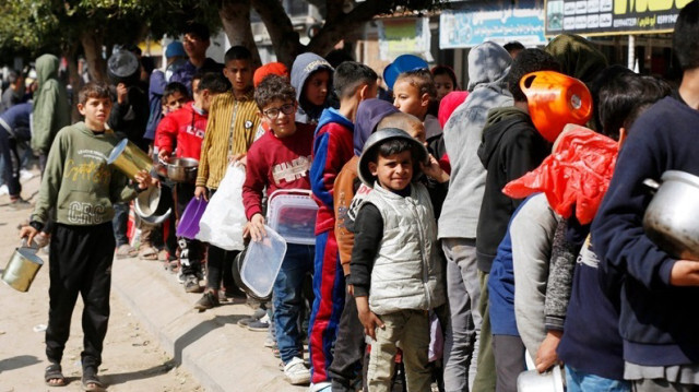 Des enfants palestiniens, avec des récipients vides, attendent dans une file d'attente de la nourriture, distribuée par des organisations caritatives à Gaza, le 24 février 2024.