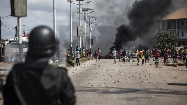 Un officier de police regarde les manifestants faire des gestes et jeter des pierres, lors d'une manifestation de masse le matin après la publication des résultats préliminaires pour cinq communes à Conakry, le 21 octobre 2020. 