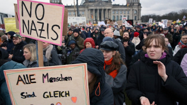 Un participant montre des pancartes sur lesquelles on peut lire "Pas de nazis" et "Tous les êtres humains sont égaux" lors d'un rassemblement contre la politique de droite devant le bâtiment du Reichstag à Berlin, en Allemagne, le 3 février 2024.