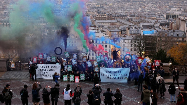 Les membres du groupe "Le Revers de la Médaille" allument des fusées éclairantes et tiennent des banderoles portant les inscriptions: "Ne laissez pas l'exclusion être votre héritage" et "Jeux olympiques 2024 : le revers de la médaille", près de la Basilique du Sacré-Cœur, à Paris le 15 décembre 2023.