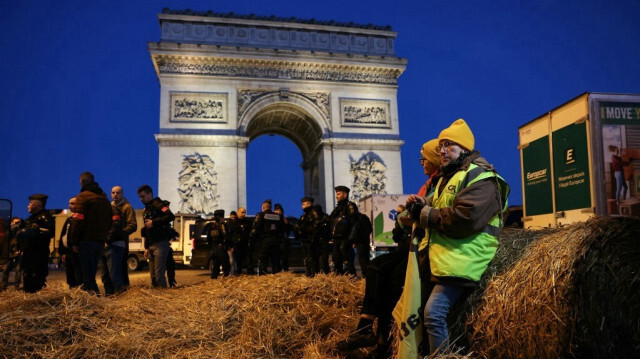 Des agriculteurs français assis sur des bottes de foin pendant que des policiers surveillent la zone devant l'Arc de Triomphe, près de l'avenue des Champs-Élysées, lors d'une manifestation du syndicat des agriculteurs français à Paris, le 1er mars 2024.