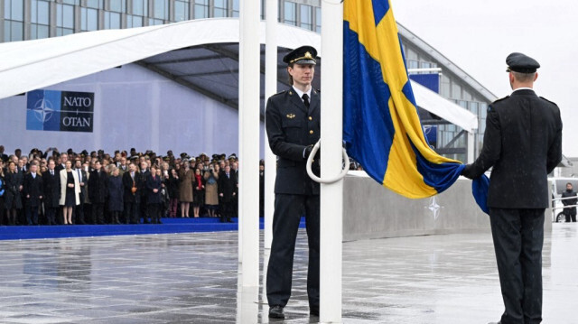 Des fonctionnaires en train de hisser le drapeau national suédois sur un mât lors de la cérémonie d'adhésion de la Suède à l'OTAN au siège de l'Alliance de l'Atlantique Nord à Bruxelles, le 11 mars 2024.