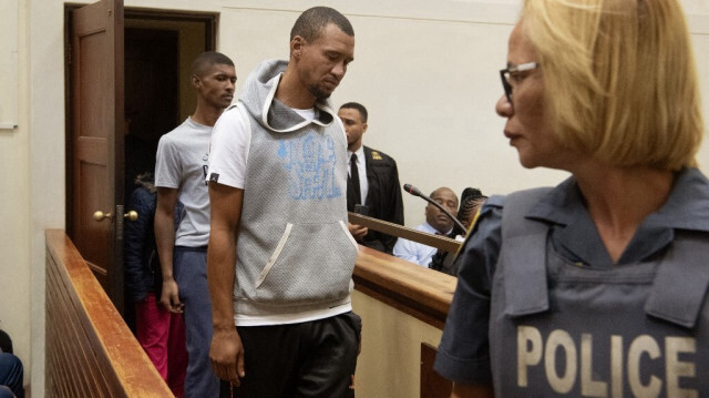 Un officier de la police sud-africaine (SAPS) regarde les accusés Stevano van Rhyn (à gauche) et Jacquen Appollis entrer dans la salle d'audience du tribunal de première instance de Vredenburg, le 13 mars 2024, où l'affaire de la disparition de Joshlin Rachelin Smith est jugée. 