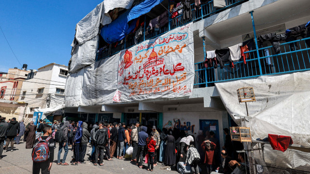 Une grande feuille affichant un message de bienvenue pour le mois sacré musulman du Ramadan est suspendue à un bâtiment où les Palestiniens se rassemblent pour recevoir de l'aide humanitaire, dans un camp abritant des Palestiniens déplacés érigé dans une école gérée par l'Office de secours et de travaux des Nations Unies pour les réfugiés de Palestine (UNRWA) à Rafah, dans le sud de la bande de Gaza, le 13 mars 2024.
