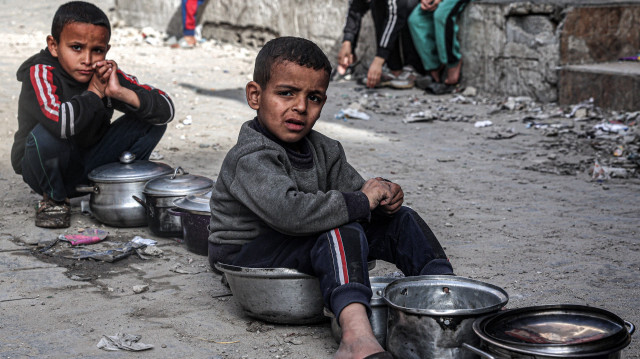 Des garçons assis avec des pots vides alors que des Palestiniens déplacés font la queue pour recevoir des repas fournis par une organisation caritative avant le repas "iftar" de rupture du jeûne pendant le mois sacré musulman du Ramadan, à Rafah dans le sud de la bande de Gaza, le 16 mars 2024, dans le cadre du conflit actuel sur le territoire palestinien entre Israël et le groupe militant du Hamas.