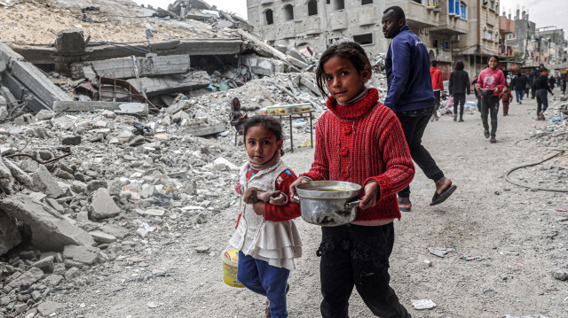 Des enfants passant devant les décombres d'un bâtiment effondré avec un pot de nourriture fourni par une organisation caritative avant le repas de rupture du jeûne "iftar" pendant le mois sacré musulman du Ramadan, à Rafah dans le sud de la bande de Gaza le 16 mars 2024, dans le cadre du conflit actuel sur le territoire palestinien entre Israël et le groupe militant du Hamas.
