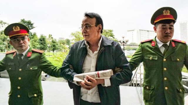 Le président du groupe Tan Hoang Minh, Do Anh Dung (C), est escorté par des policiers jusqu'au tribunal pour son procès pour fraude, à Hanoi, le 19 mars 2024.