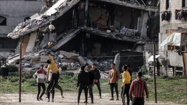 Палестинская молодежь, укрывающаяся в лагере Нусейрат от нападений израильской армии, играет в волейбол возле частично разрушенного здания в ожидании ифтара в священный месяц Рамадан в Дейр аль-Балах, сектор Газа, 27 марта 2024 года.