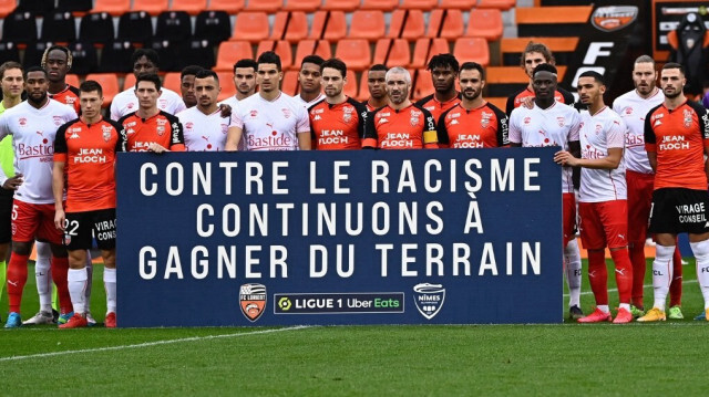 Des joueurs tiennent une banderole "contre le racisme, nous continuerons à gagner du terrain" avant le début du match de football de L1 entre le FC Lorient et le Nîmes Olympique, au stade du Moustoir à Lorient, dans le nord-ouest de la France, le 13 décembre 2020.
