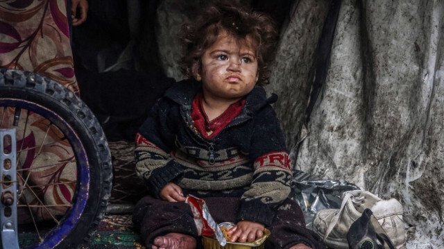 Un enfant palestinien déplacé de force à cause des bombardements de l'armée d'occupation israélienne, assis sous un abri de fortune près d'une rue à Rafah, le 14 mars 2024.