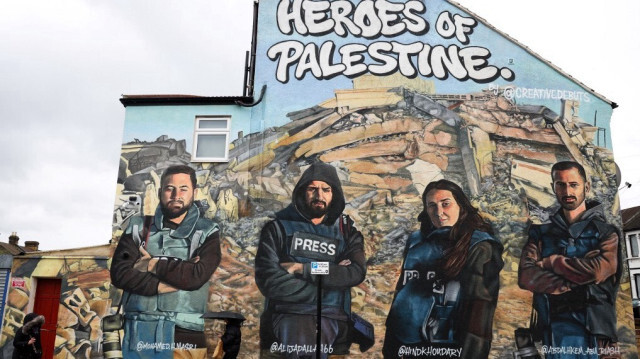 Un piéton passe devant une peinture murale réalisée par les artistes de rue Auberi Chen, Core 246 et Captain Kris représentant les photographes palestiniens Mohammed Al-Masri (G), Ali Jadallah (2e G), Abdelhakim Abu Riash (D) et la journaliste palestinienne Hind Khoudary (2e D) à Ilford, dans l'est de Londres, le 27 mars 2024, dans le cadre d'un projet lancé par la plateforme artistique Creative Debuts et intitulé "Héros de la Palestine".