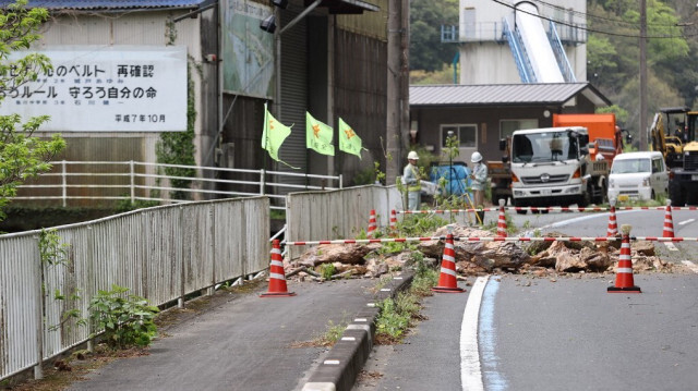 Les travailleurs regardent une section fermée de la route nationale après que des rochers sont tombés de l'autre côté de la route lorsqu'un tremblement de terre de magnitude 6,3 a frappé le sud du Japon tard dans la nuit précédente, dans la ville d'Ozu, dans la préfecture d'Ehime, le 18 avril 2024.