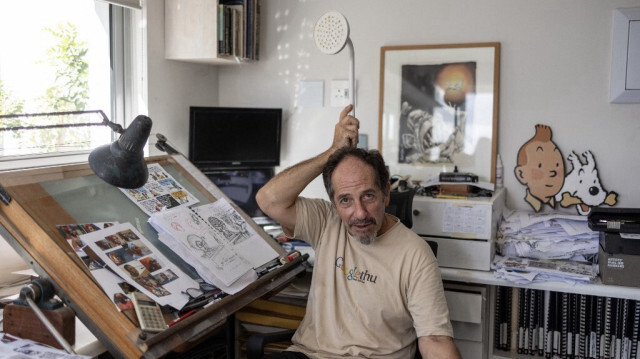 Le dessinateur sud-africain Jonathan Shapiro, connu sous le nom de Zapiro, tient une pomme de douche au-dessus de sa tête alors qu'il pose pour une photo dans son studio du Cap, le 4 avril 2024. 