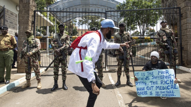 Un médecin kenyan (C), rejoint par un activiste, chante devant le siège du ministère de la santé en manifestant avec des pancartes pour demander de meilleurs salaires et conditions de travail dans la capitale, Nairobi, le 16 avril 2024. 
