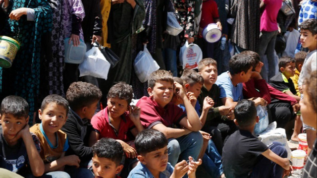 Des enfants palestiniens font la queue avec leurs récipients vides pour recevoir des repas chauds fournis par des organisations caritatives alors que l'embargo israélien se poursuit dans la Bande de Gaza.