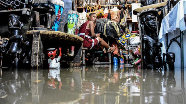 Une employée est assise à l'intérieur de son magasin avec l'eau inondée de la rivière Msimbazi après qu'elle ait débordé, après des pluies continues ,au marché de Vinyago à Dar es Salaam, le 17 décembre 2019.