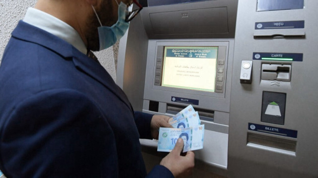 Un homme récupère des billets de banque tunisiens nouvellement mis en circulation dans un distributeur automatique de billets à Tunis, le 27 mars 2020.
