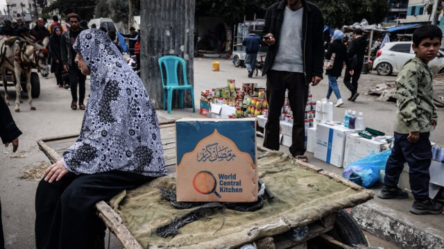 Une femme palestinienne assise sur un chariot à côté d'une boîte de rations alimentaires fournies par l'organisation caritative World Central Kitchen à un marché de rue improvisé à Rafah, dans le sud de la bande de Gaza, le 14 mars 2024.