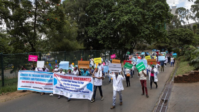 Des travailleurs de la santé manifestent le long d'une rue avec des pancartes à Nairobi le 20 mars 2024 pour réclamer l'emploi permanent que le gouvernement kenyan leur avait assuré après trois ans de service.