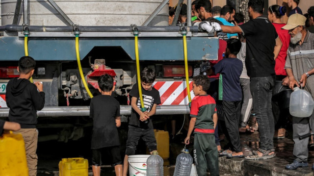 Des enfants remplissent des jerrycans et des récipients d'eau à partir de la citerne d'un camion-citerne dans un camp abritant des Palestiniens déplacés à Rafah, dans le sud de la bande de Gaza, le 30 avril 2024.