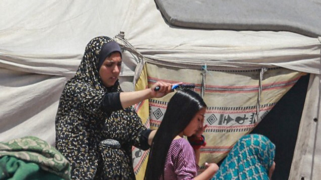 Une femme palestinienne déplacée brosse les cheveux d'une fillette à l'extérieur d'une tente à Khan Yunis, dans le sud de la bande de Gaza, le 9 mai 2024.