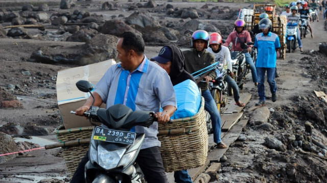 Des personnes conduisent leurs motos sur un sentier de fortune fait de dalles de bois pour éviter la boue causée par des inondations soudaines dans le village de Rambatan, Tanah Datar Regency, Sumatra Ouest, le 14 mai 2024.